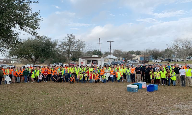 Large group photo of many people in work vests at a park with a small Salvation Army trailer in back