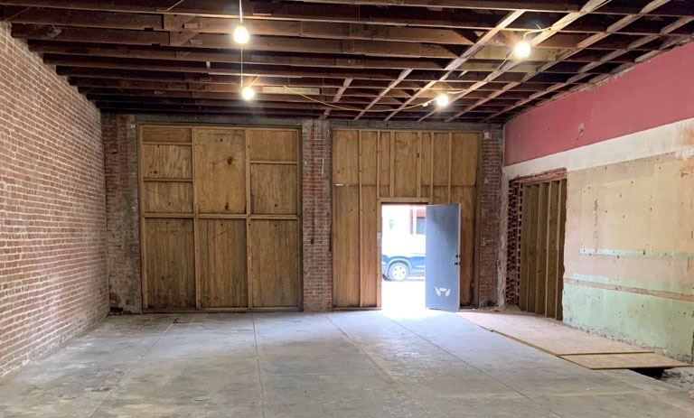 An empty building with brick walls, plywood surrounding door frame and bare ceiling
