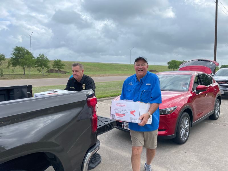 A man in a blue work shirt and a uniformed police officer load boxes into a pickup truck