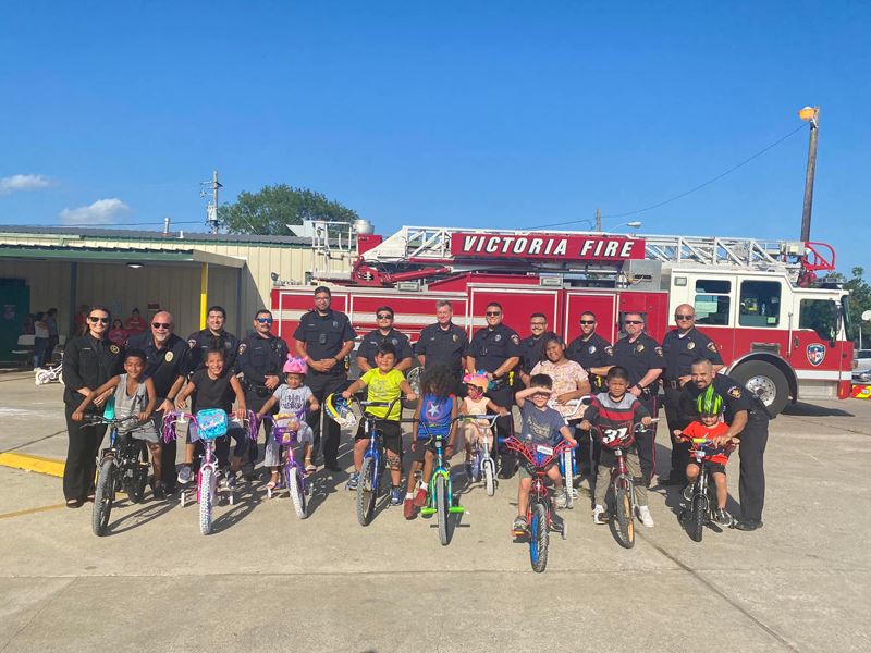 Group photo with kids on bikes and uniformed police officers in front of a fire truck