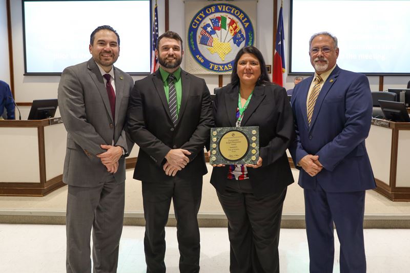 Group photo of four people at Council chambers. One holds a plaque.