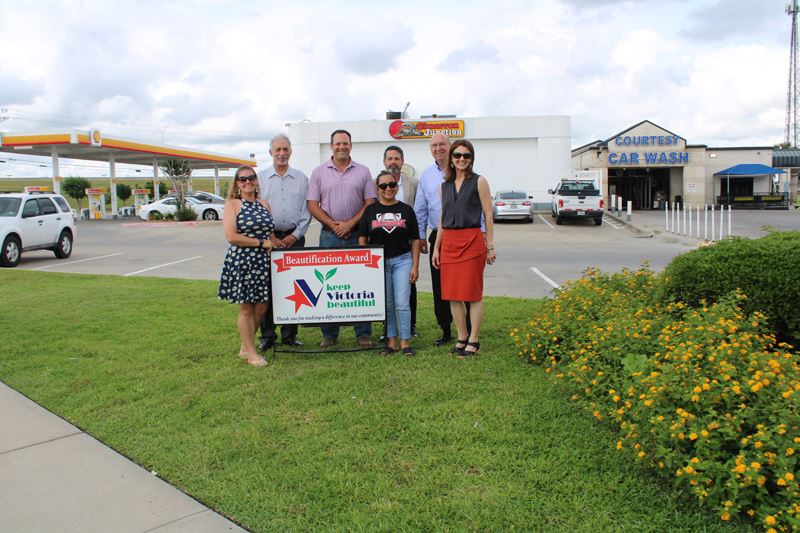 Group photo with KVB sign in front of Cimarron Junction convenience store near bed of yellow flowers