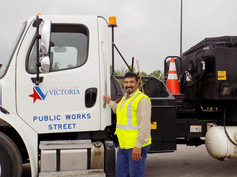 Smiling Public Works employee in a safety vest in front of a truck labeled Public Works Street