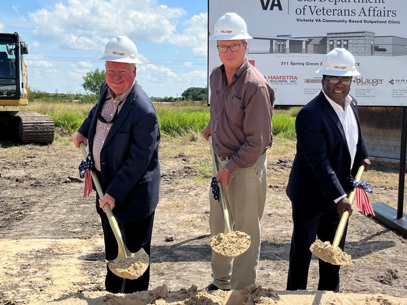 Three people hold shovelfuls of dirt in gold shovels