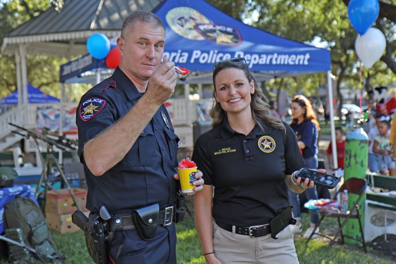 A uniformed policeman holding a snow cone and a woman in a police polo pose for a picture