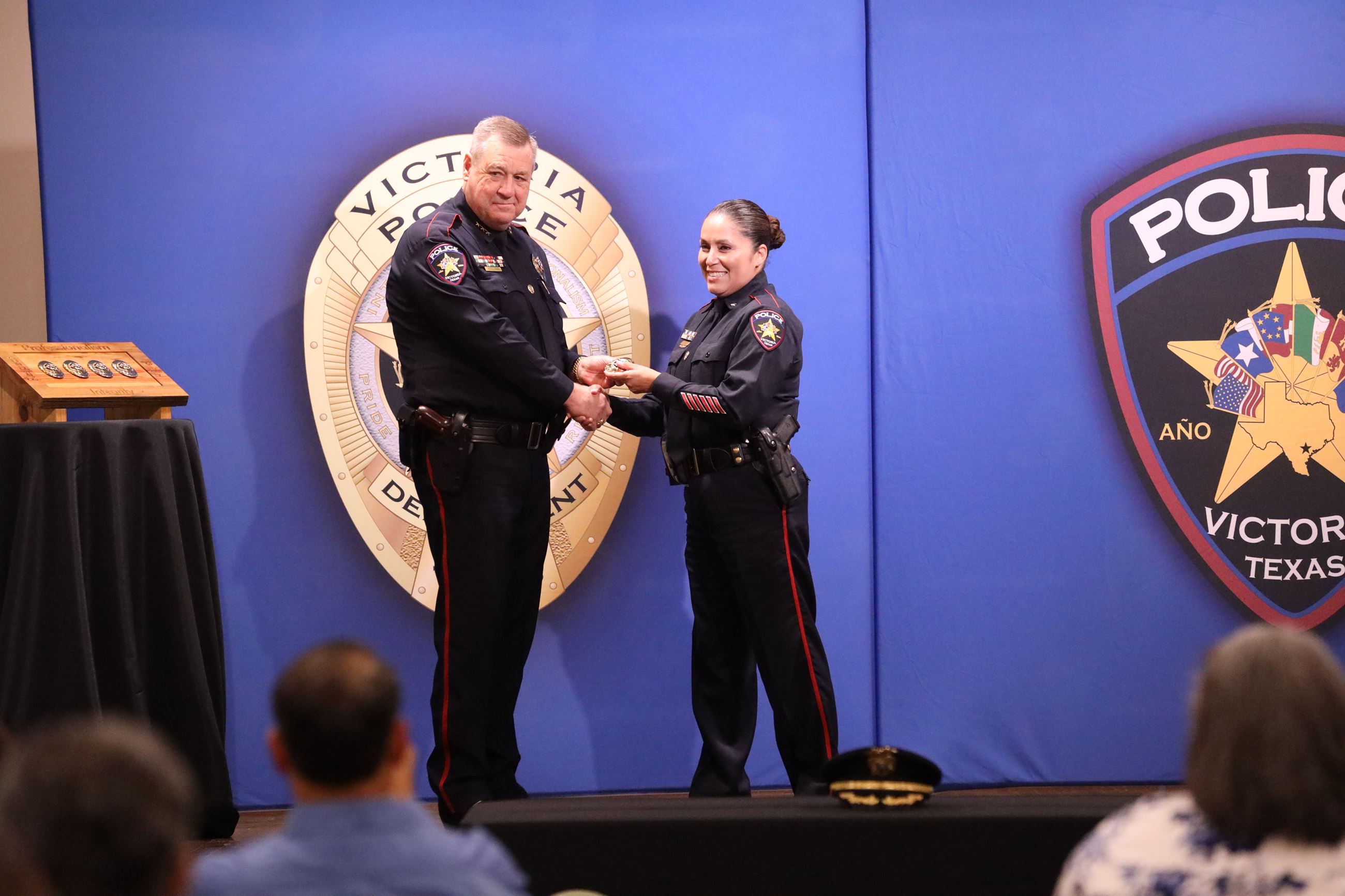 Uniformed policeman hands a badge to uniformed policewoman and shakes her hand