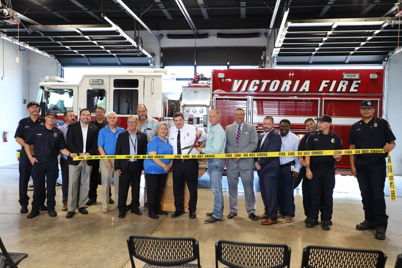 Officials hold up a piece of caution tape to cut with novelty scissors in front of a fire truck