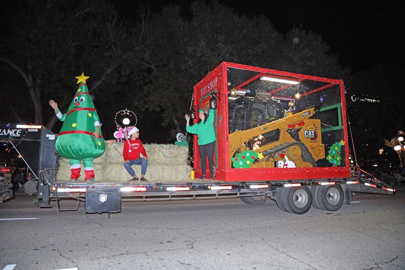 A parade float with heavy machinery in a toy shop, elves, a Christmas tree character