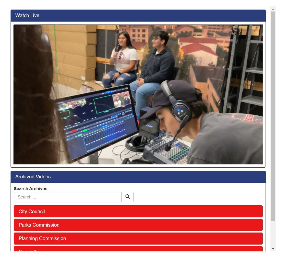 Two students sit in chairs in front of a Texas State backdrop. Another student works a sound board.