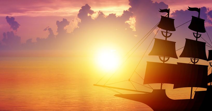 An old-fashioned sailing ship on the ocean silhouetted by a sunset