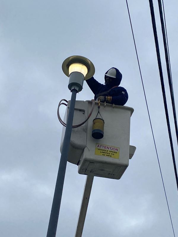 Technician in a cherry picker basket turns on a post top streetlight.