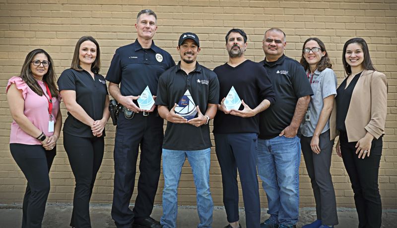 Group photo of eight people. Three of them hold trophies.