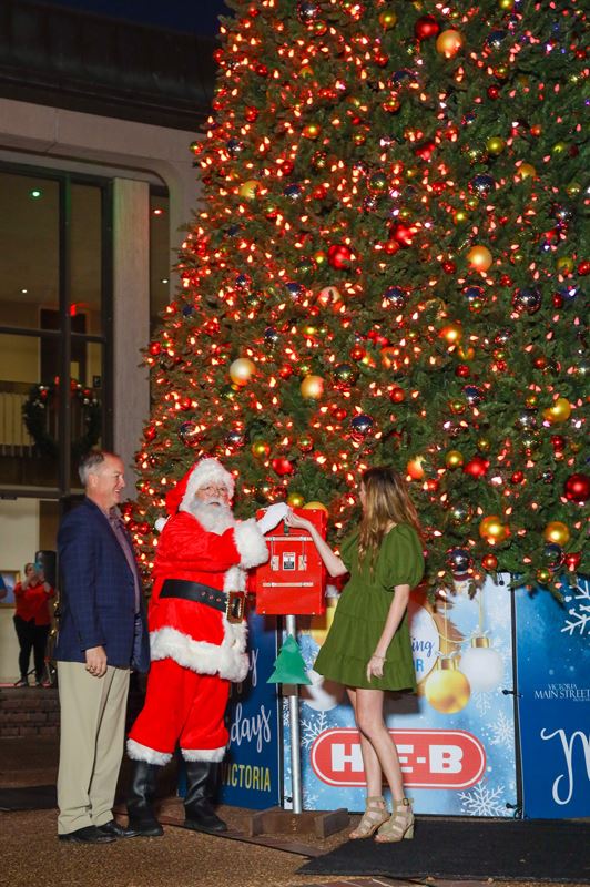 Santa Claus and a young woman prepare to throw a ceremonial light switch on a Christmas tree