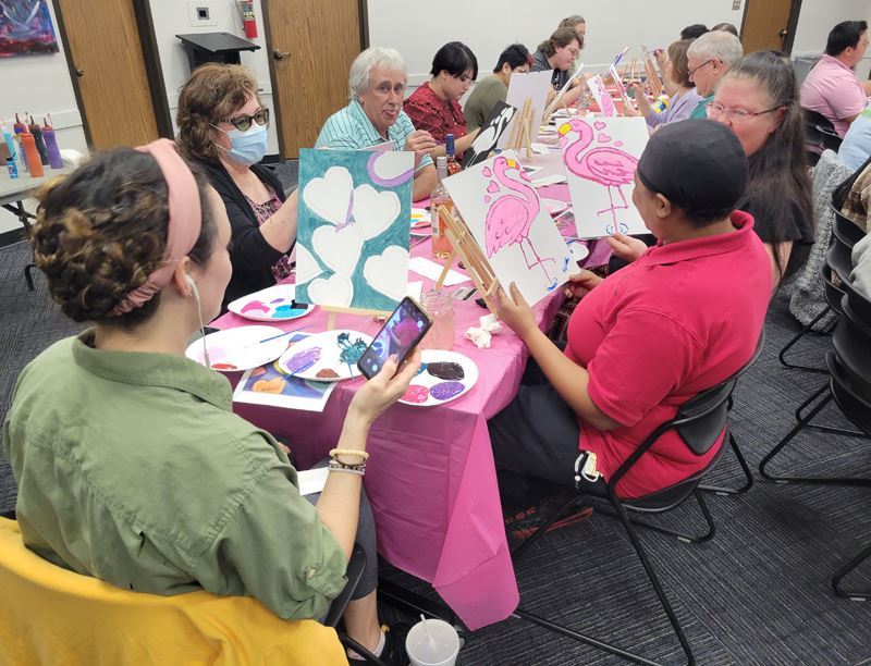 Adults seated around a table making paintings of flamingos and hearts