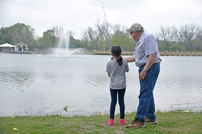 A man helps a girl fish in the duck pond