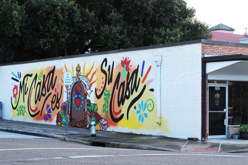 Mural with the phrase Mi Casa es Su Casa, floral imagery, a cross and a Sacred Heart symbol