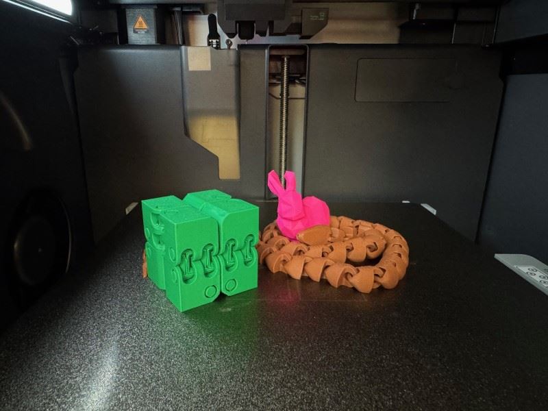 Three items created from a 3D printer including a rabbit, an articulated cube, and a snake.