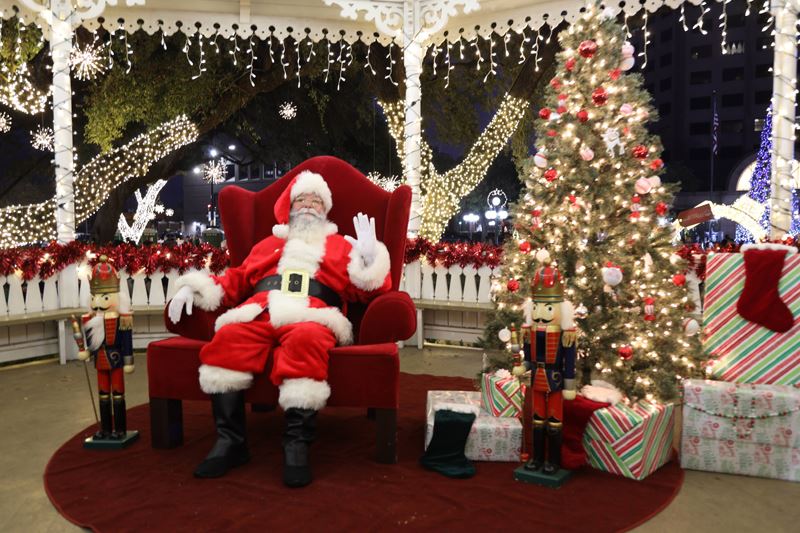 Santa Claus seated in a chair by a Christmas tree in the De Leon Plaza bandstand