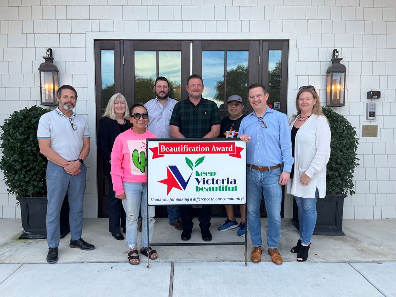 Group photo with KVB sign in front of double doors between two ficuses and decorative lamps