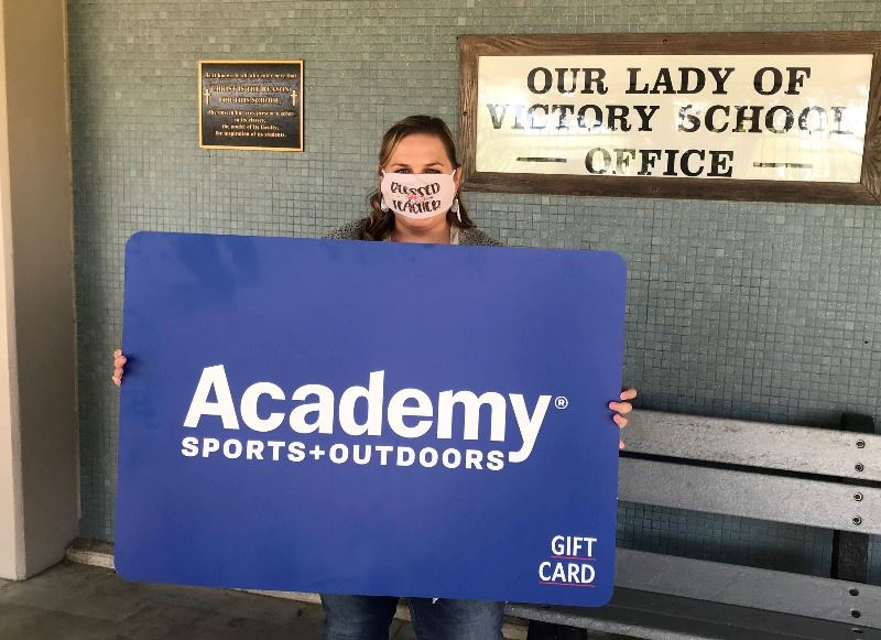 Woman holds giant Academy Sports and Outdoors gift card