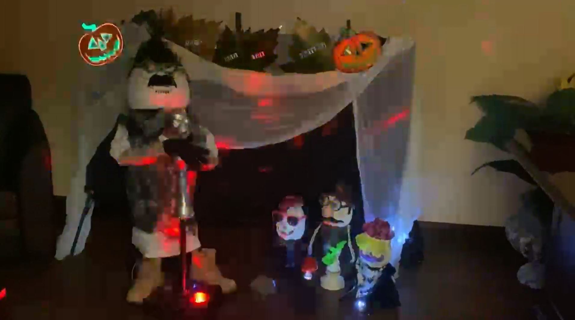 A mustached pumpkin man and smaller pumpkin people in strobe lighting