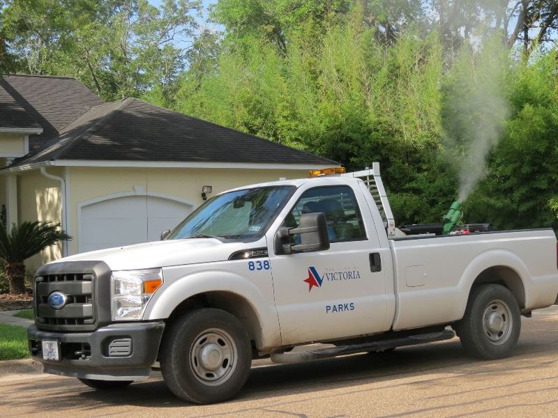 A truck with a Parks & Recreation logo sprays a white foggy pesticide in a neighborhood.