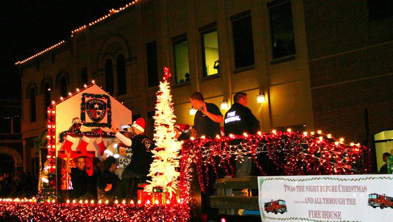 People wave from lighted parade float decorated with lights, VFD logo and fireplace