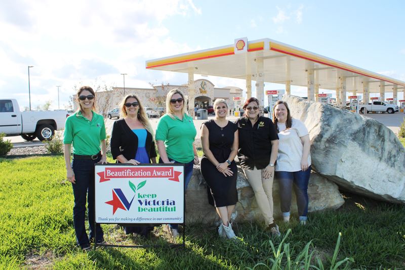 Group photo with KVB logo sign and landscaping boulders. There is a gas station in the background.