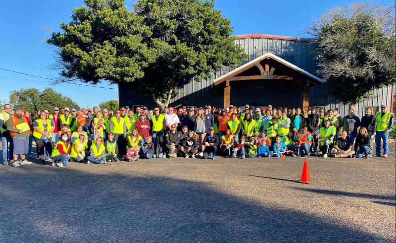Large group of people, most wearing safety vests, pose for a photo in front of a church