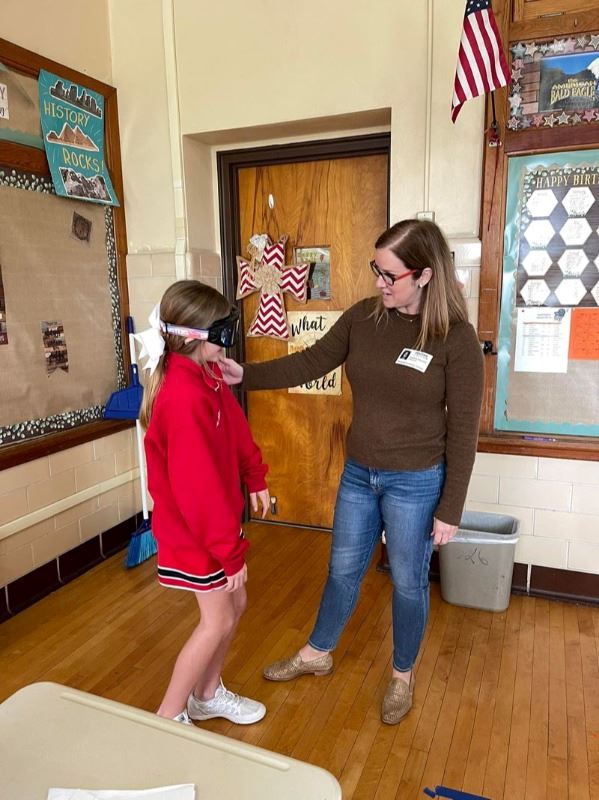 A woman places her hand on the shoulder of a girl wearing dark goggles.