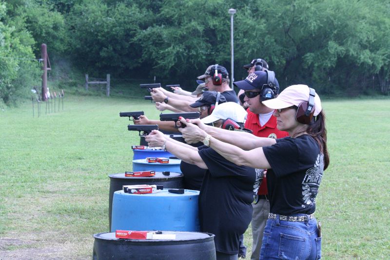 A row of people at an outdoor shooting range fire guns