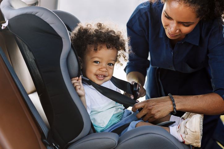Woman buckles a happy baby into a car seat