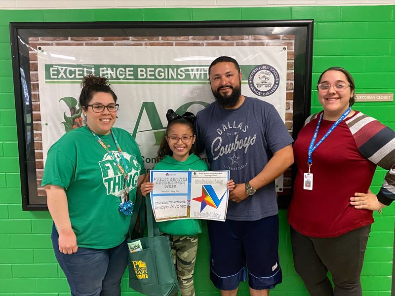 Group photo of 3 adults and 1 child holding a coloring page with a colorful City of Victoria star.