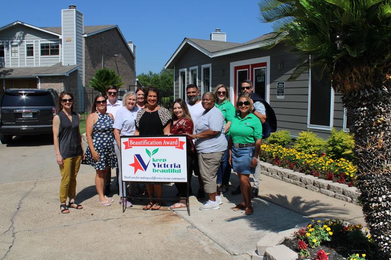 Group photo in front of apartment office landscaped with flowers and a palm tree