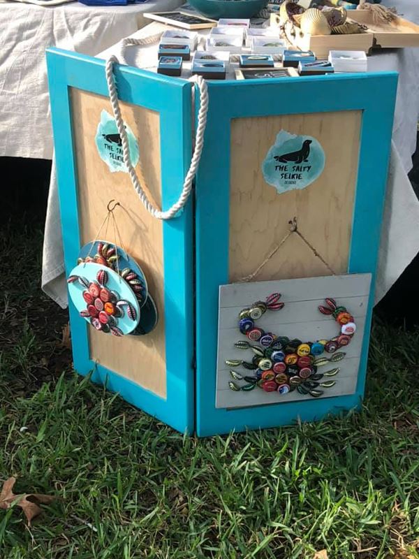 Wall hanging decorations of sea creatures made of bottlecaps are displayed at an outdoor market.