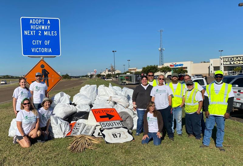Group poses with collected trash bags near Adopt a Highway sign