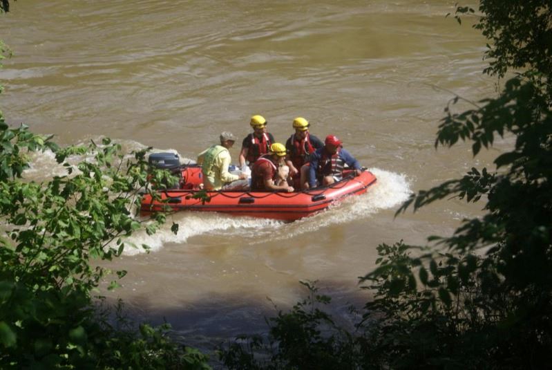 five rescue personnel in an orange raft on the river practice rescue boat operations