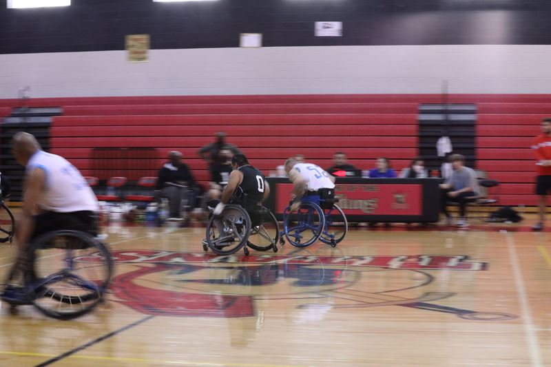 People in wheelchairs and basketball jerseys move around a basketball court