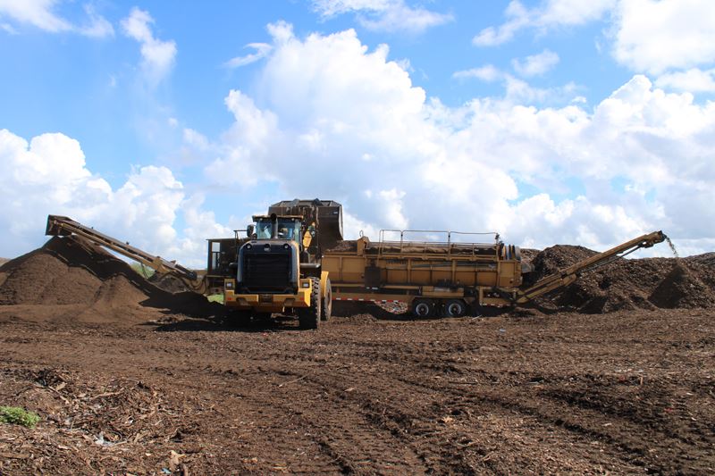 A big yellow machine spits out coarse wood chips on one side and fine compost on the other.
