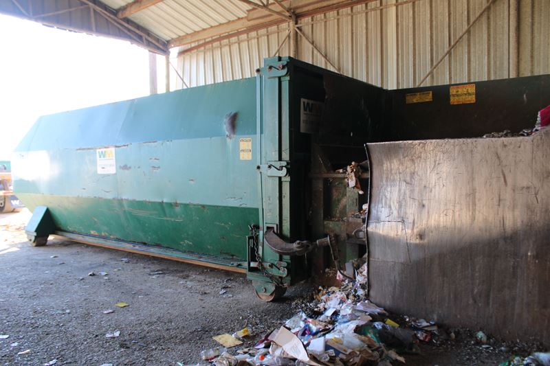 A large green rectangular machine with waste spilling out the corner