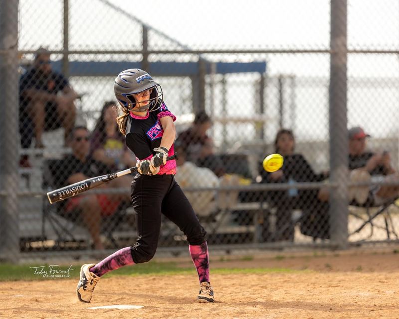 Softball player swings a bat at a ball Opens in new window
