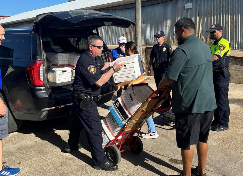 A uniformed police officer loads boxes of paper from the back of a vehicle onto a dolly.
