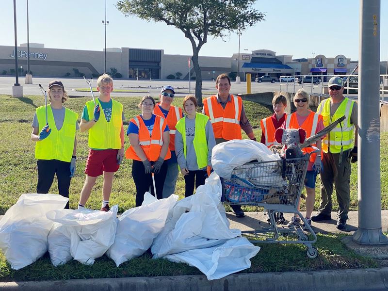 People in work vests near the mall with trash bags and a cart full of trash and a toy elephant.