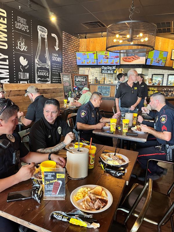 People in police shirts and uniforms sit and eat barbecue plates in a restaurant