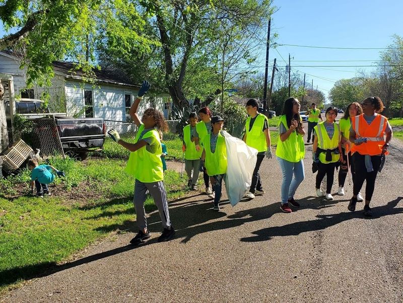 A group in safety vests, mostly teens, walk down a residential street