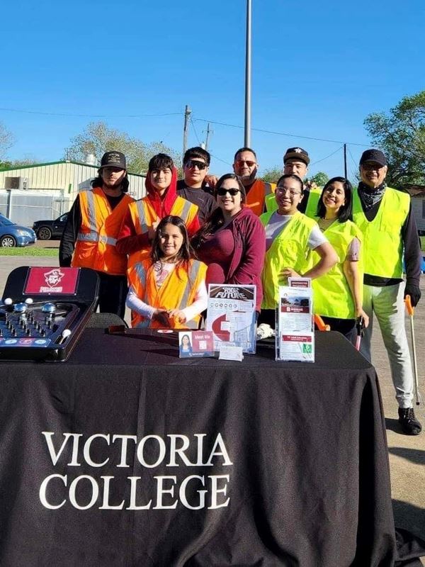 A group in safety vests stand at a table with a Victoria College tablecloth