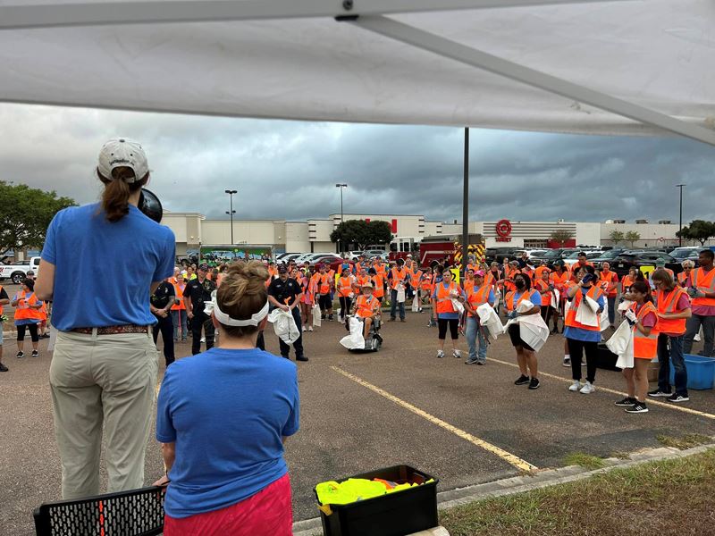 A woman with a megaphone addresses a crowd of people in safety vests Opens in new window
