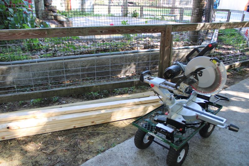 A large circular saw and a pile of fresh two-by-fours sit near a fence