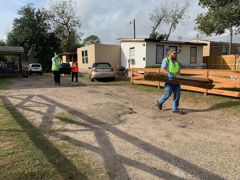 Volunteers in safety vests haul wood and trash away from a home