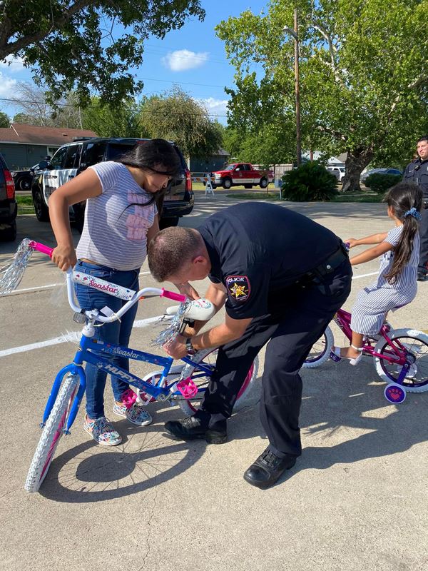 A man in police uniform adjusts a child's bike seat.